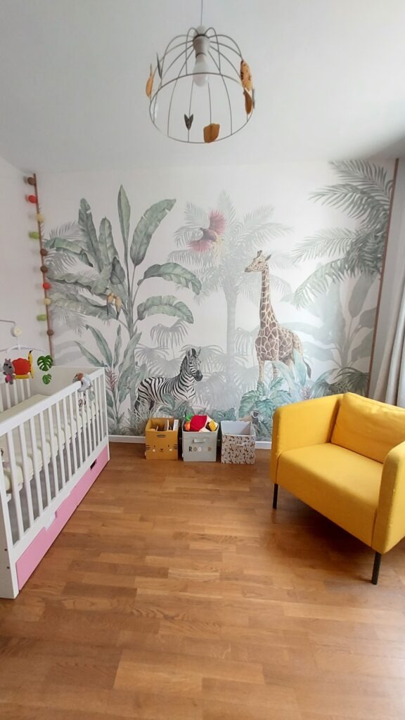 photo d'une chambre bébé, dans les tons jaune et beige, avec un papier peint jungle de couleurs pastels