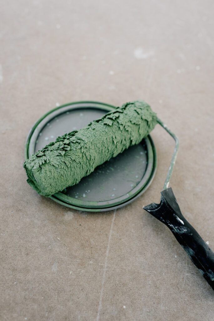 rouleau de peinture, imbibé de peinture verte, posé sur le couvercle du pot de peinture