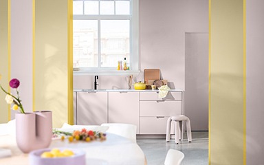 Cette photo représente une cuisine, où tout est rose : mur, cuisine, tabouret. Deux bandeaux jaune encadrent la cuisine