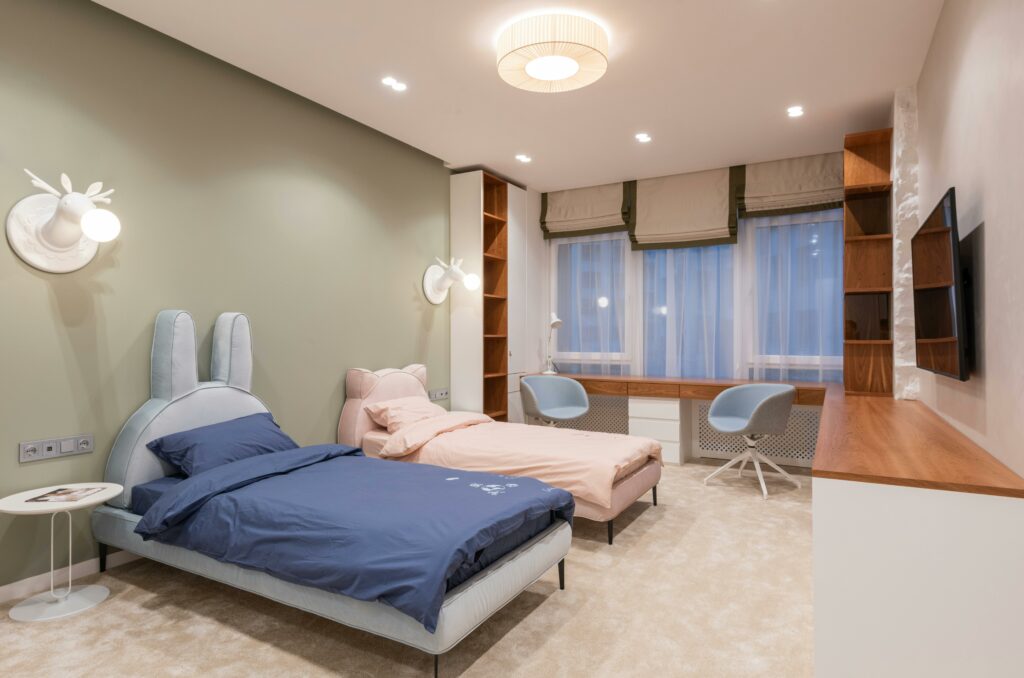 Aménager une chambre partagée pour deux enfants : lits bleu et rose avec têtes de lit lapin et bureaux jumeaux distincts face à la fenêtre.