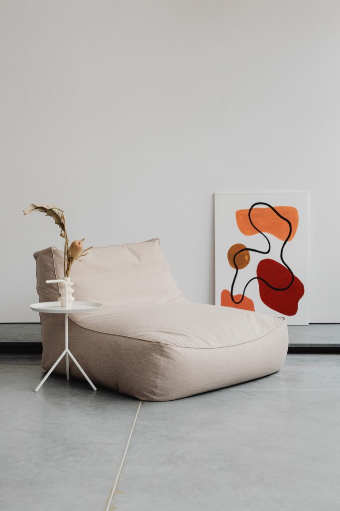 Fauteuil beige et mur neutre avec tableau coloré posé au sol — reprendre sa place et son identité dans son intérieur grâce à un élément de couleur fort